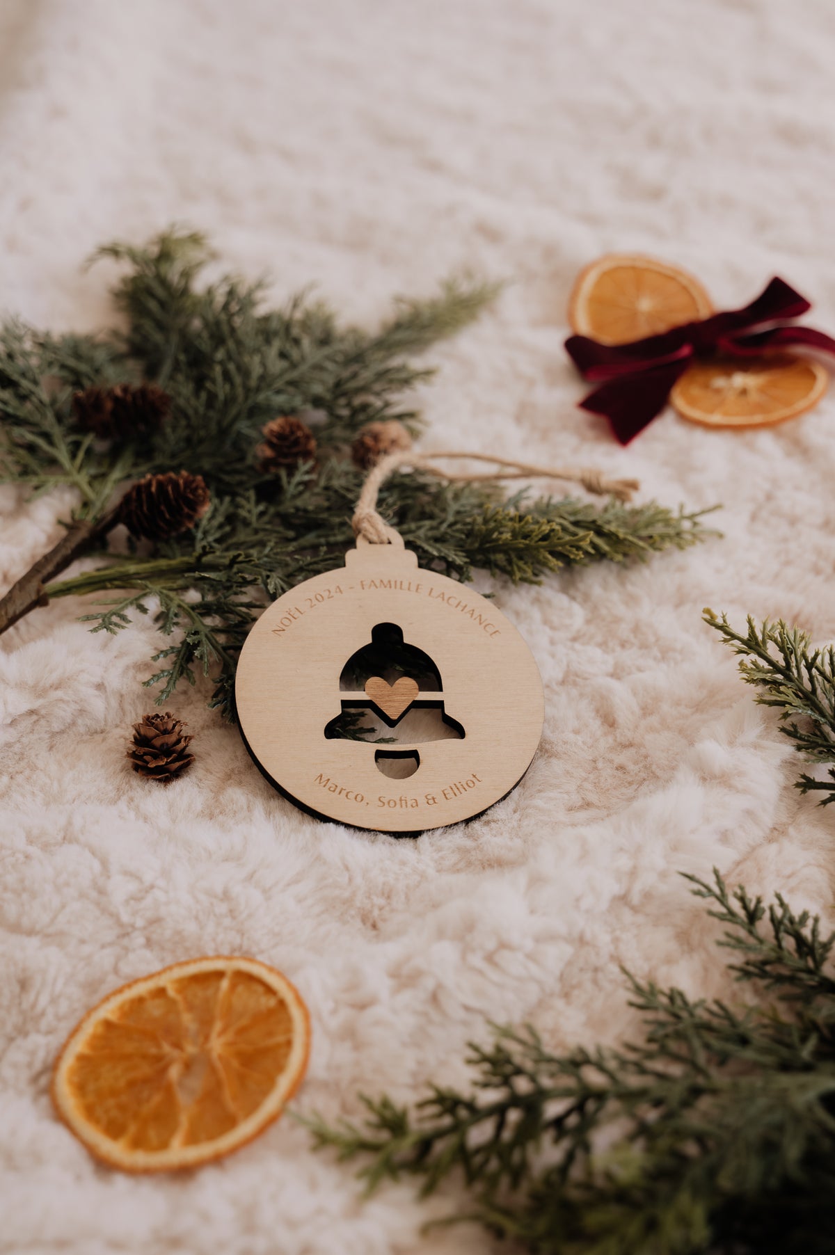 Boule de Noël personnalisée - Découpe : cloche ajourée avec cœur central, entourée de sapin et d’oranges séchées.