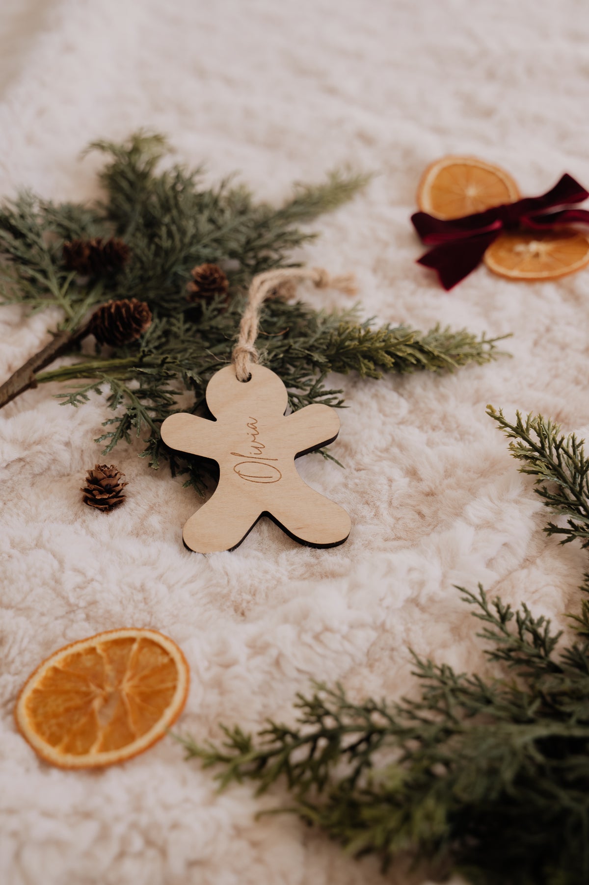 Ornement personnalisé - Pain d’épice : bonhomme en bois gravé Olivia, sur une couverture crème avec sapin et oranges.