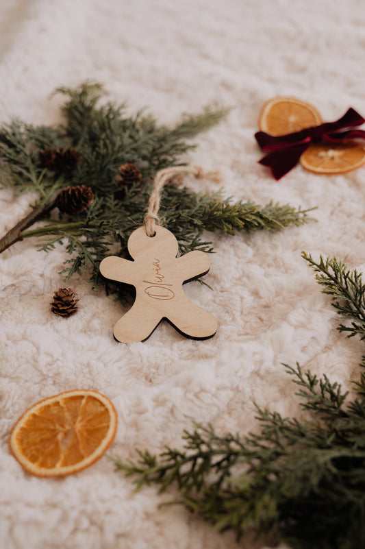 Ornement personnalisé - Pain d’épice : bonhomme en bois gravé Olivia, sur une couverture crème avec sapin et oranges.