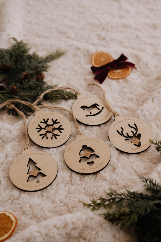 Boule de Noël personnalisée - Découpe : cinq modèles en bois sur une couverture crème, avec sapin et oranges séchées.