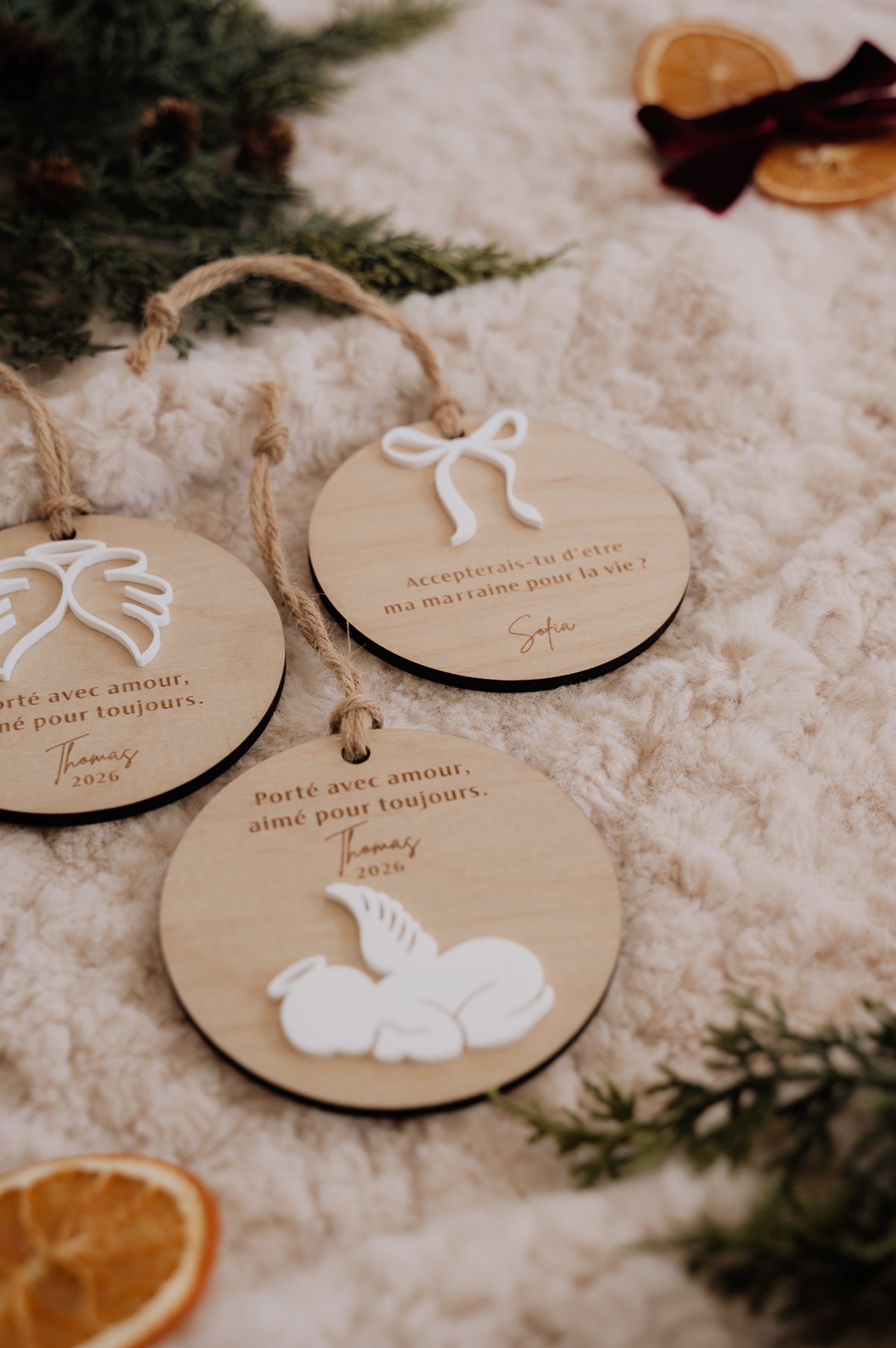Boule de Noël personnalisée - Superposée : trois modèles sur une couverture crème, près de sapin et d’oranges séchées.