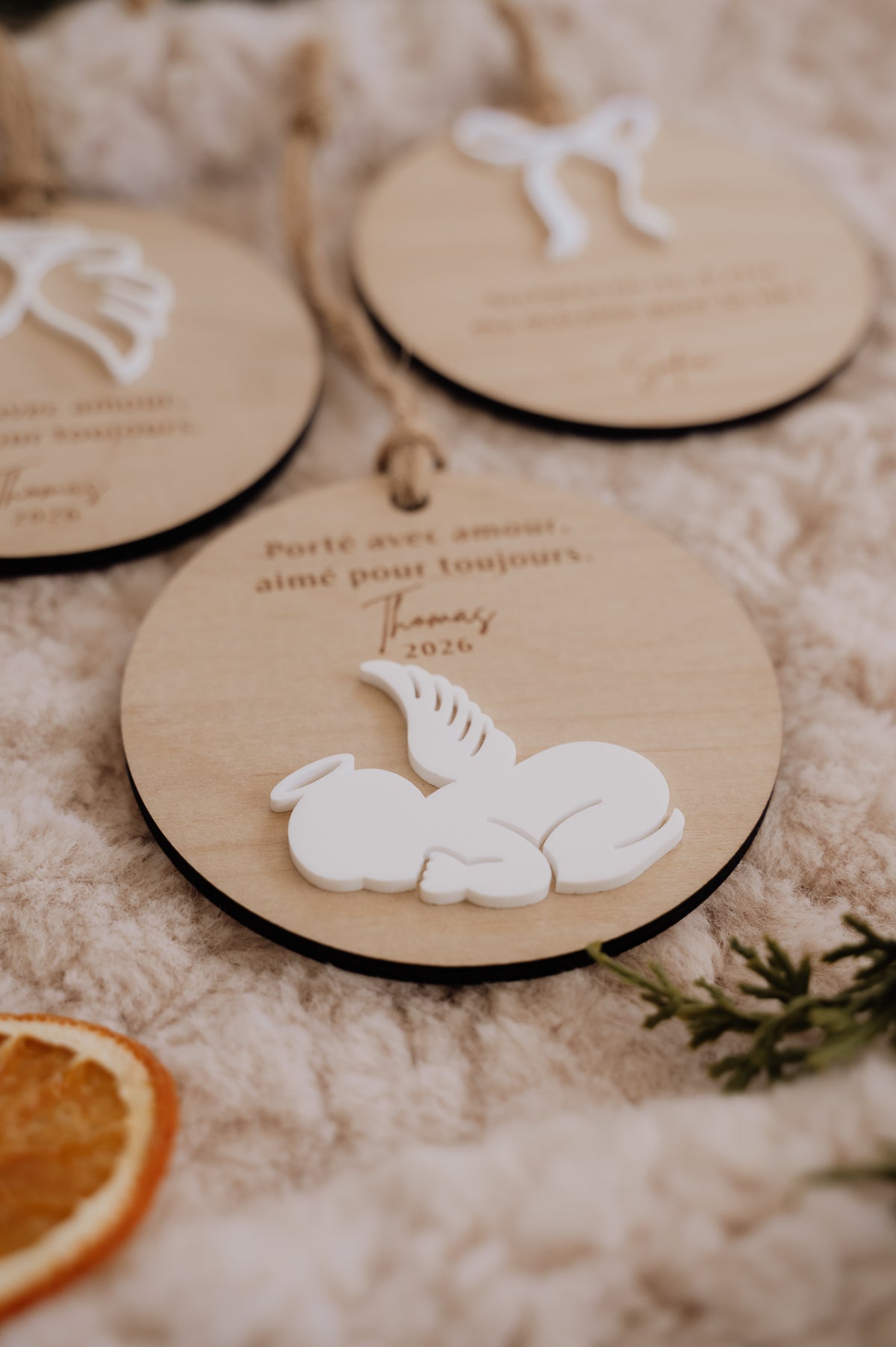 Boule de Noël personnalisée - Superposée : vue rapprochée du bébé ange blanc avec aile et auréole, sur fond de bois.