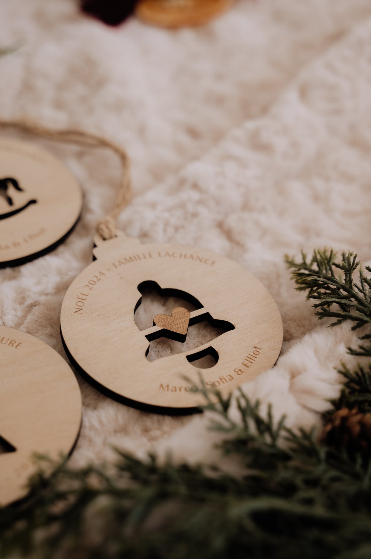 Boule de Noël personnalisée - Découpe : gros plan de la cloche ajourée et de son cœur, près d’une branche de sapin.