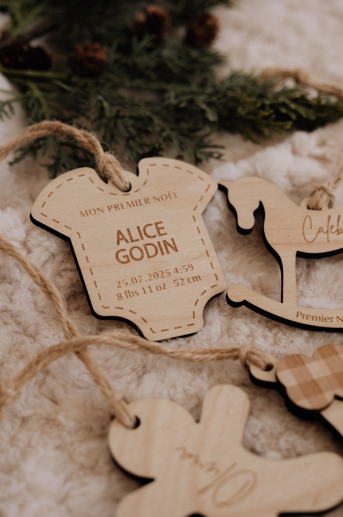 Ornement personnalisé - Cache couche : modèle Alice Godin avec cordon de jute, parmi d’autres ornements en bois.