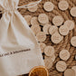 Le Sac à souvenirs : sac en coton et pastilles d’activités de Noël sur un plateau tressé, avec une orange séchée.