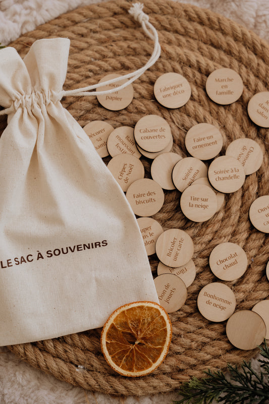 Le Sac à souvenirs : sac en coton et pastilles d’activités de Noël sur un plateau tressé, avec une orange séchée.