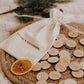 Le Sac à souvenirs : sac et pastilles en bois sur un plateau tressé, avec orange séchée et branches de sapin.