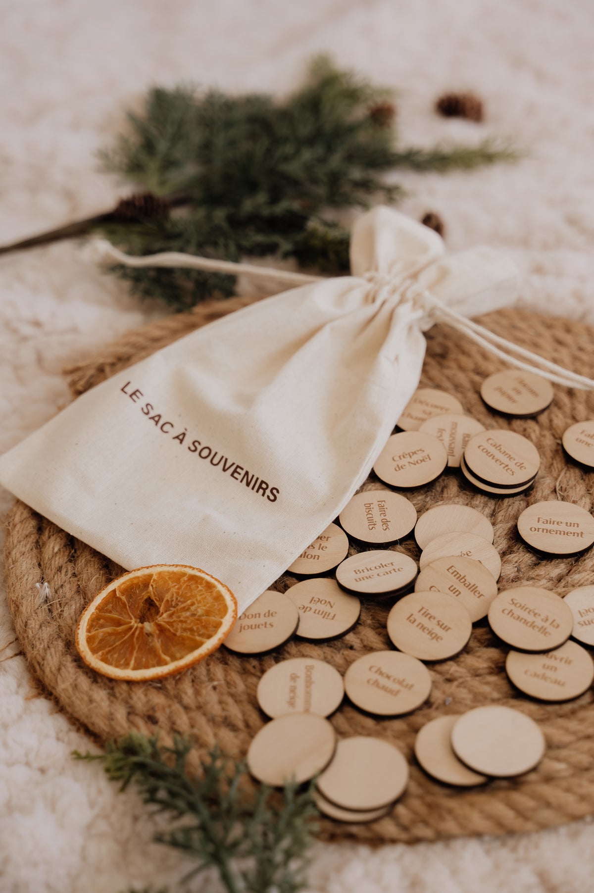 Le Sac à souvenirs : sac et pastilles en bois sur un plateau tressé, avec orange séchée et branches de sapin.
