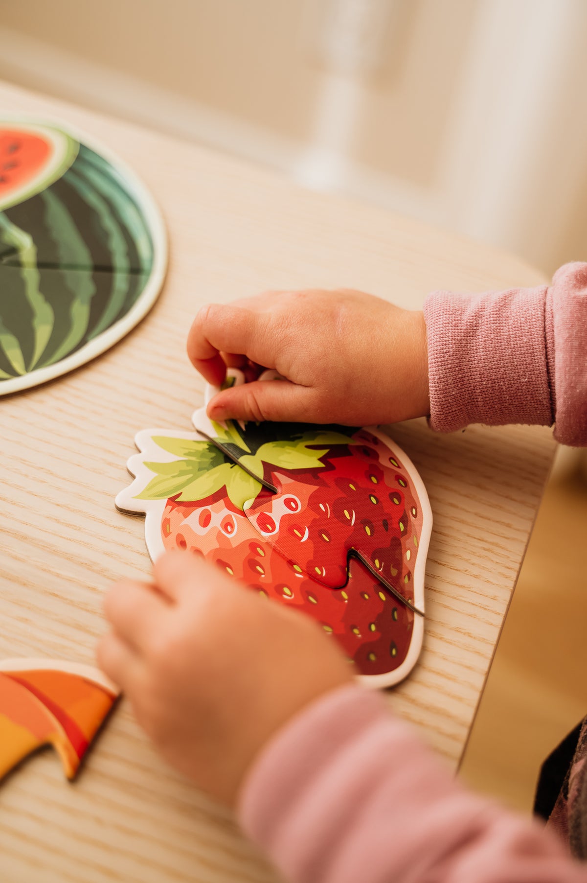 Mes premiers casse-têtes - Série Fruits : gros plan des mains d’un enfant assemblant une fraise sur une table.