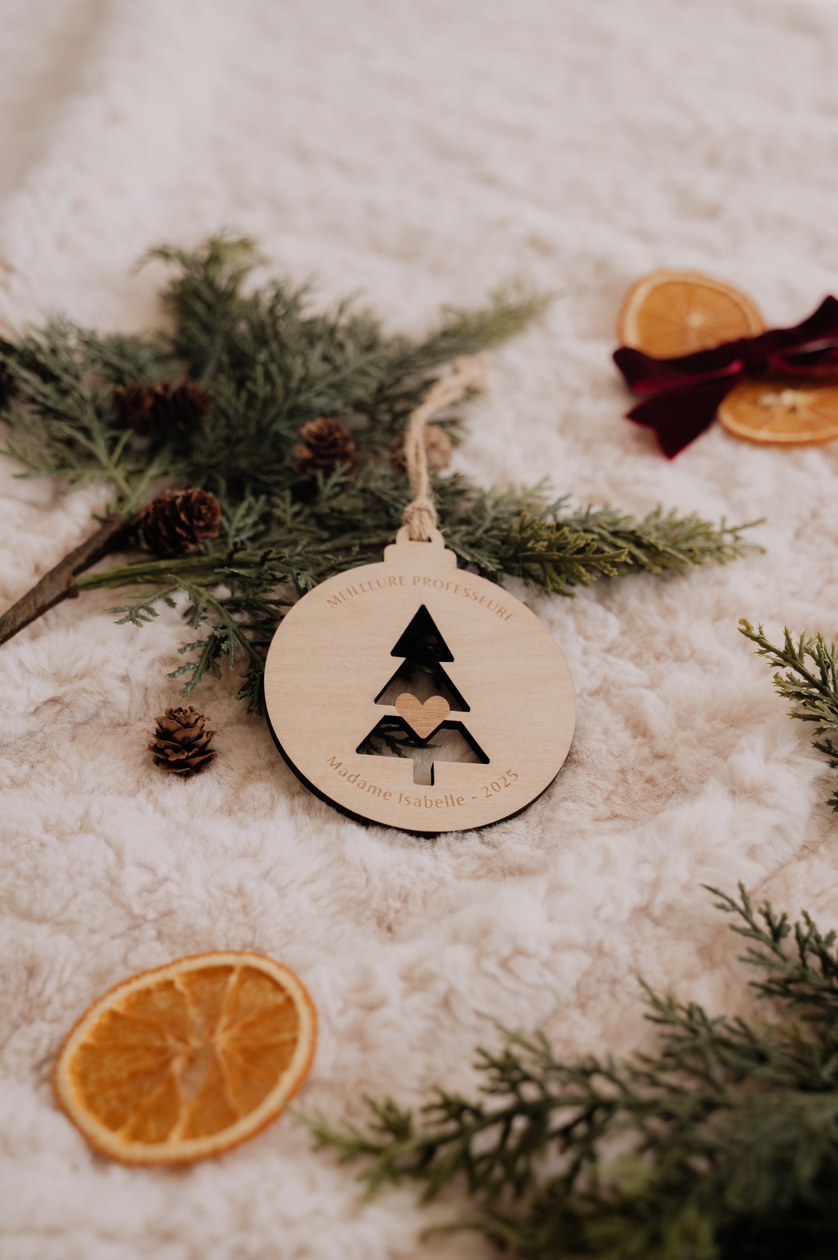 Boule de Noël personnalisée - Découpe : sapin ajouré avec cœur central, posé sur une couverture crème.
